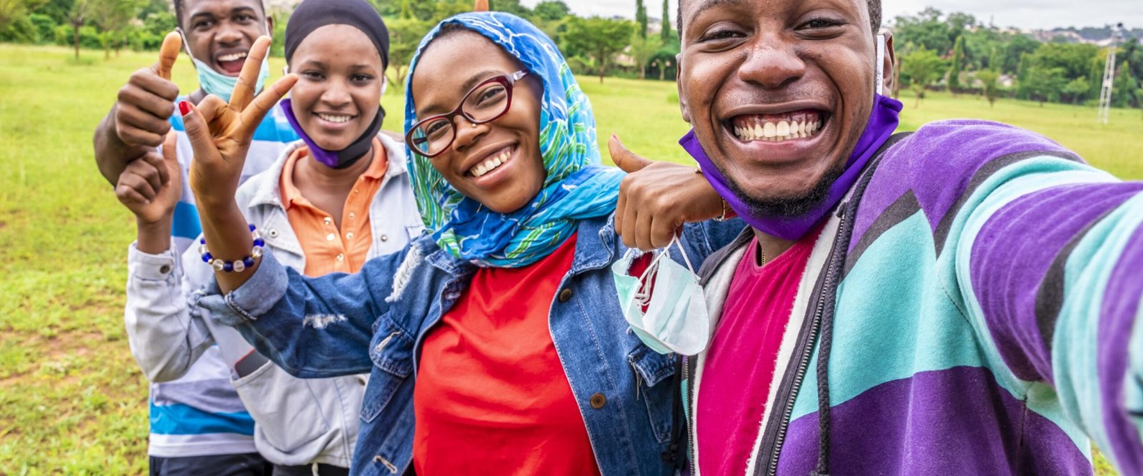 group of cheerful african friends with facemasks taking a selfie in a park